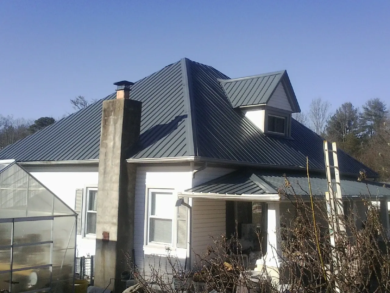Dark blue standing seam metal roof on a white farmhouse with dormer — Slate & Tile Roof Repair by Roofing Brothers in Centereach