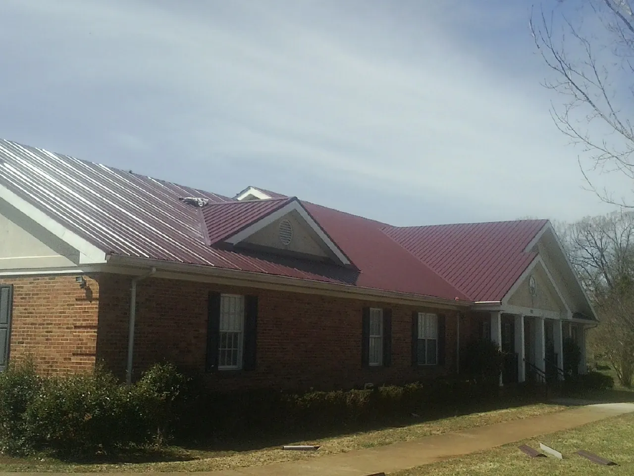Red metal roof with gabled entries on a long brick building, from a Hail Damage Roof Repair job in Centereach