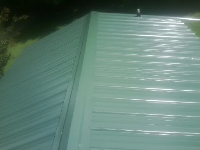 New green metal panels meeting at the ridge of a roof — Flat Roof Repair work by our crew in Centereach