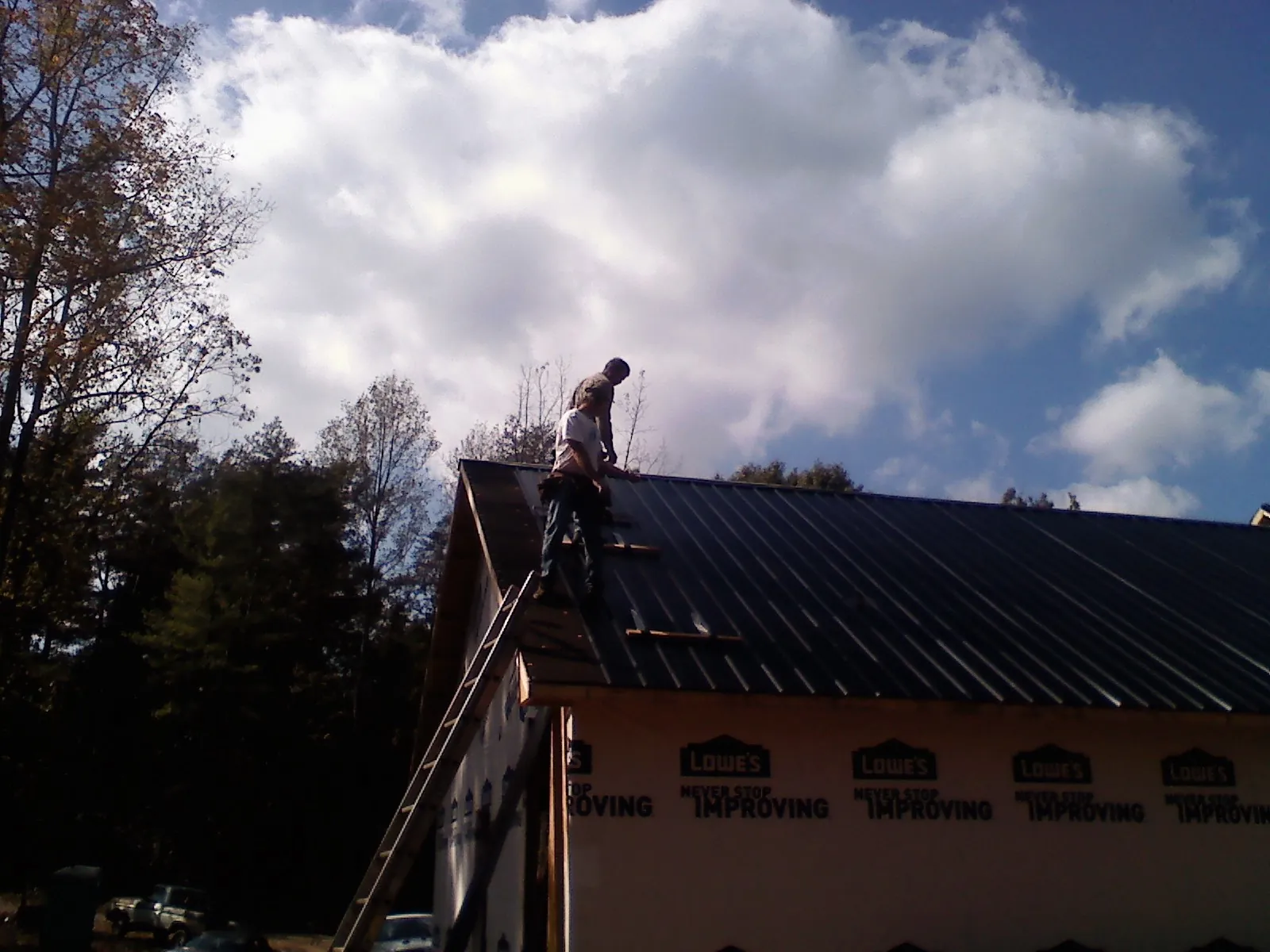 Roofer fastening dark metal panels high against a cloudy sky, from a Roof Inspection job in Centereach
