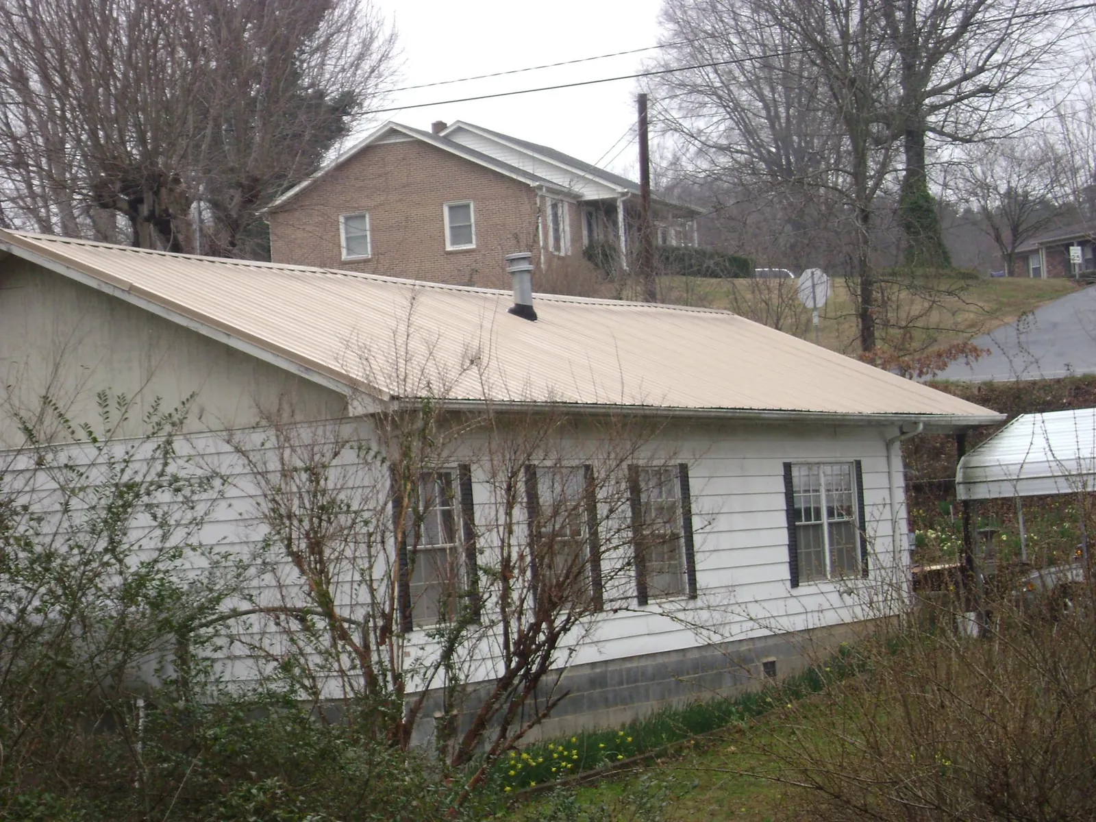 Tan metal roof on a white sided house set into a hillside — Commercial Roofing by Roofing Brothers in Centereach