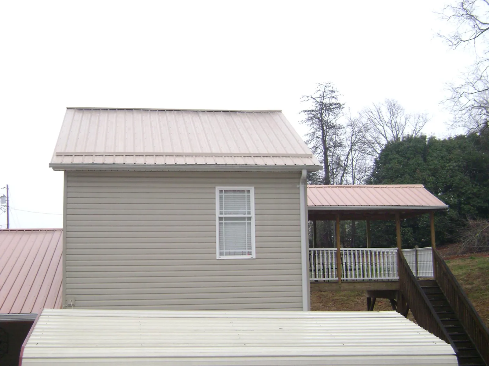 Tan metal roofs on a two story addition and attached porch, from a Roof Replacement job in Centereach
